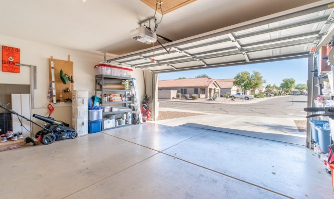 A home's garage door is wide open, revealing the surrounding neighborhood outside. Its walls feature shelves.