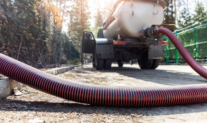 A closeup on a orange and black ribbed hose that is connected to a industrial vacuum truck in the background.