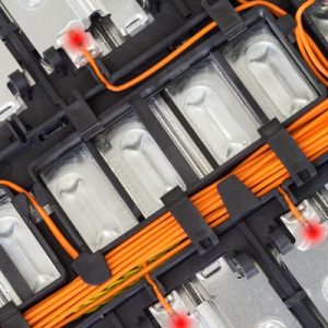 A close-up of a lithium-ion battery pack showing metal cells, orange wiring, and connectors with visible internal components.