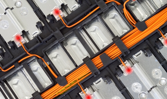 A close-up of a lithium-ion battery pack showing metal cells, orange wiring, and connectors with visible internal components.