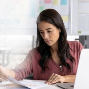 A woman working as a policy analyst in a bright home office and reviewing printed document information.