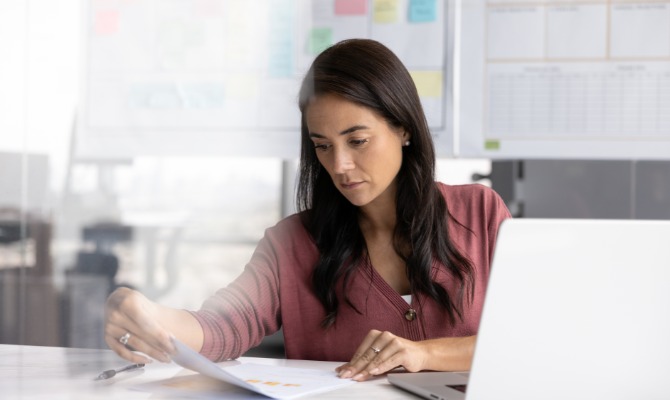 A woman working as a policy analyst in a bright home office and reviewing printed document information.