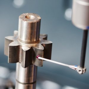 A close-up of a probe with a ruby ball tip lightly touching the edge of a gear. The probe takes the gear's measurements.
