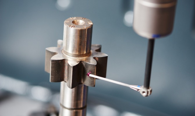 A close-up of a probe with a ruby ball tip lightly touching the edge of a gear. The probe takes the gear's measurements.