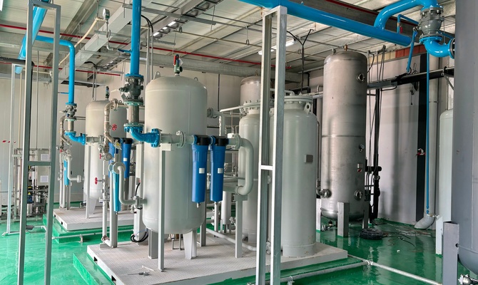 Large compressed air tanks and bright blue piping fill an industrial facility with a green floor and metal ceiling.
