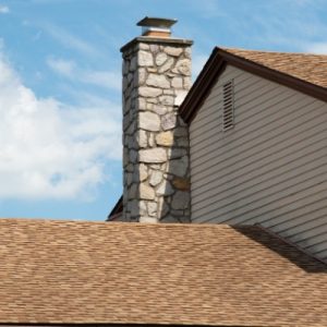 A stone chimney attached to a white painted house. The chimney has a small custom cap attached to the top.