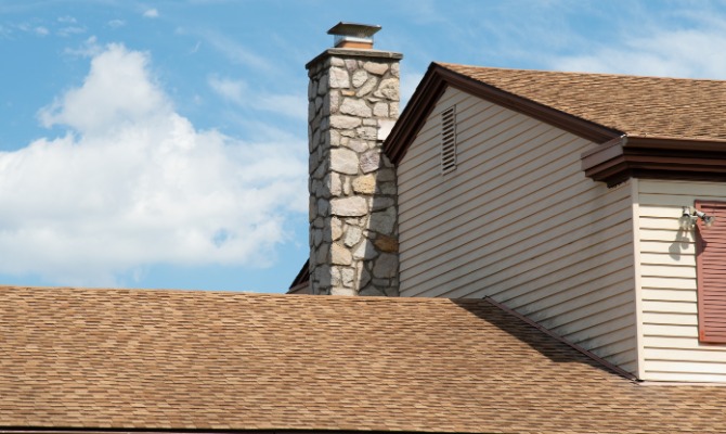 A stone chimney attached to a white painted house. The chimney has a small custom cap attached to the top.